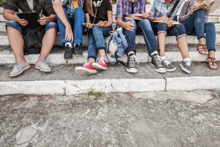 Grupa młodych studentów z książkami i gadżetami siedzi na schodach