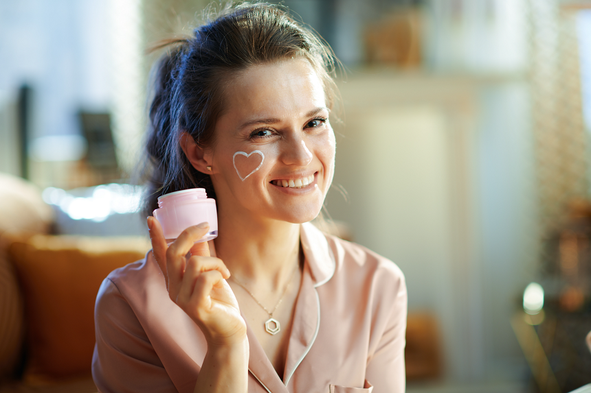 uśmiechnięta kobieta stosuje kosmetyki dermatologiczne